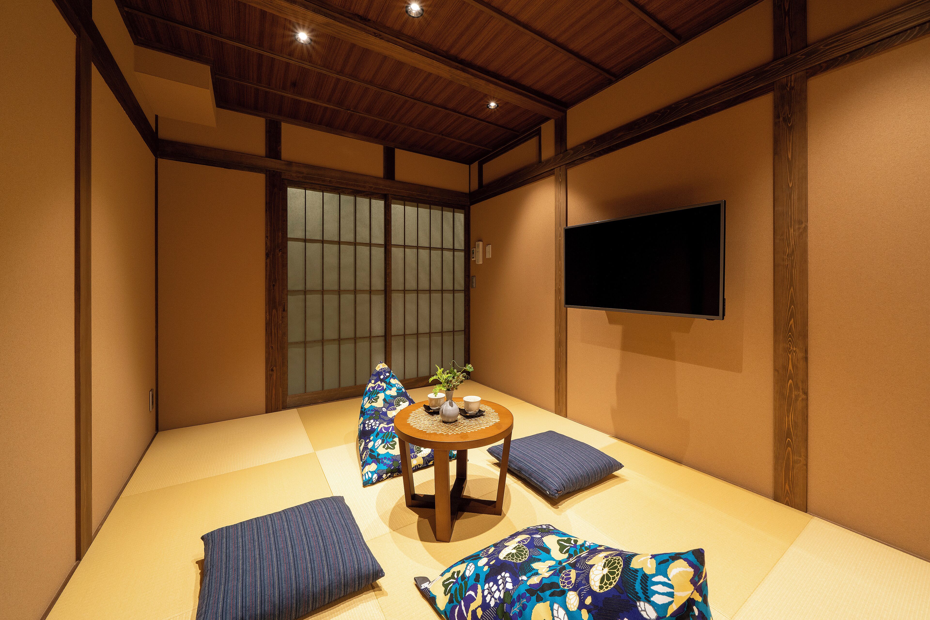 A tatami room with a low table, cushions, and a TV on the wall.