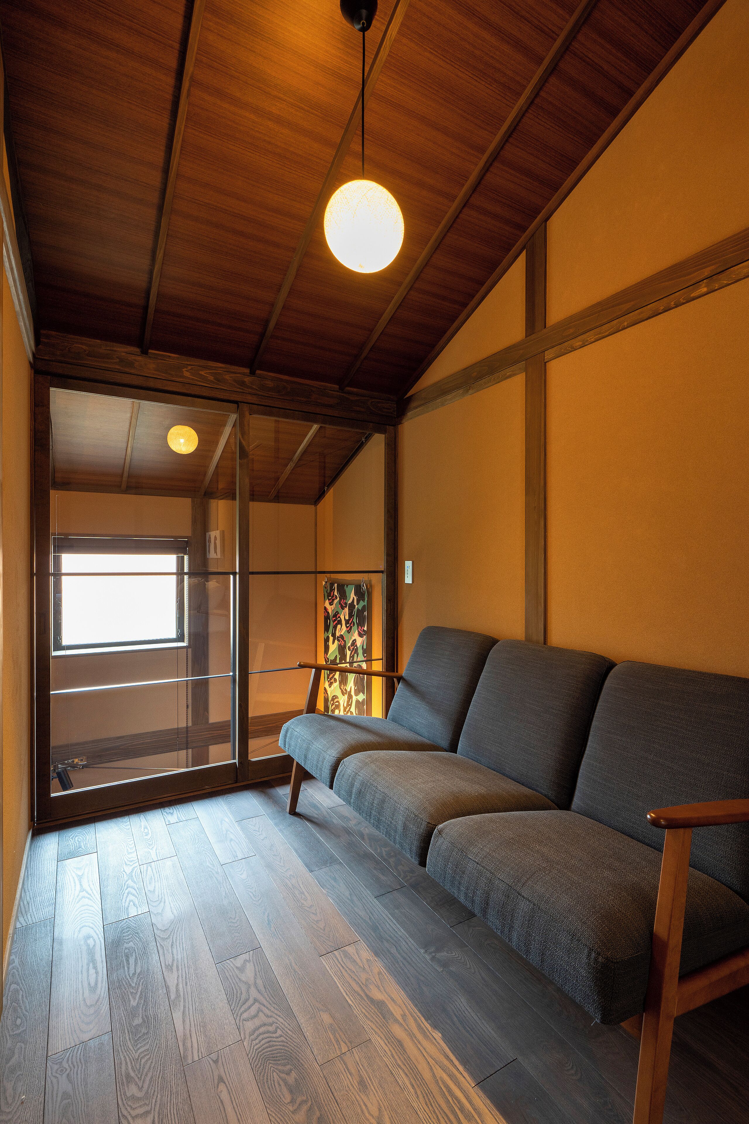 Une pièce avec un plafond en bois, un canapé et une porte-fenêtre coulissante donnant sur un balcon.