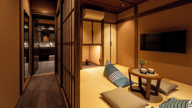 Une pièce de style japonais traditionnel, avec un sol recouvert de tatamis, une petite table basse avec des coussins et un téléviseur fixé au mur.