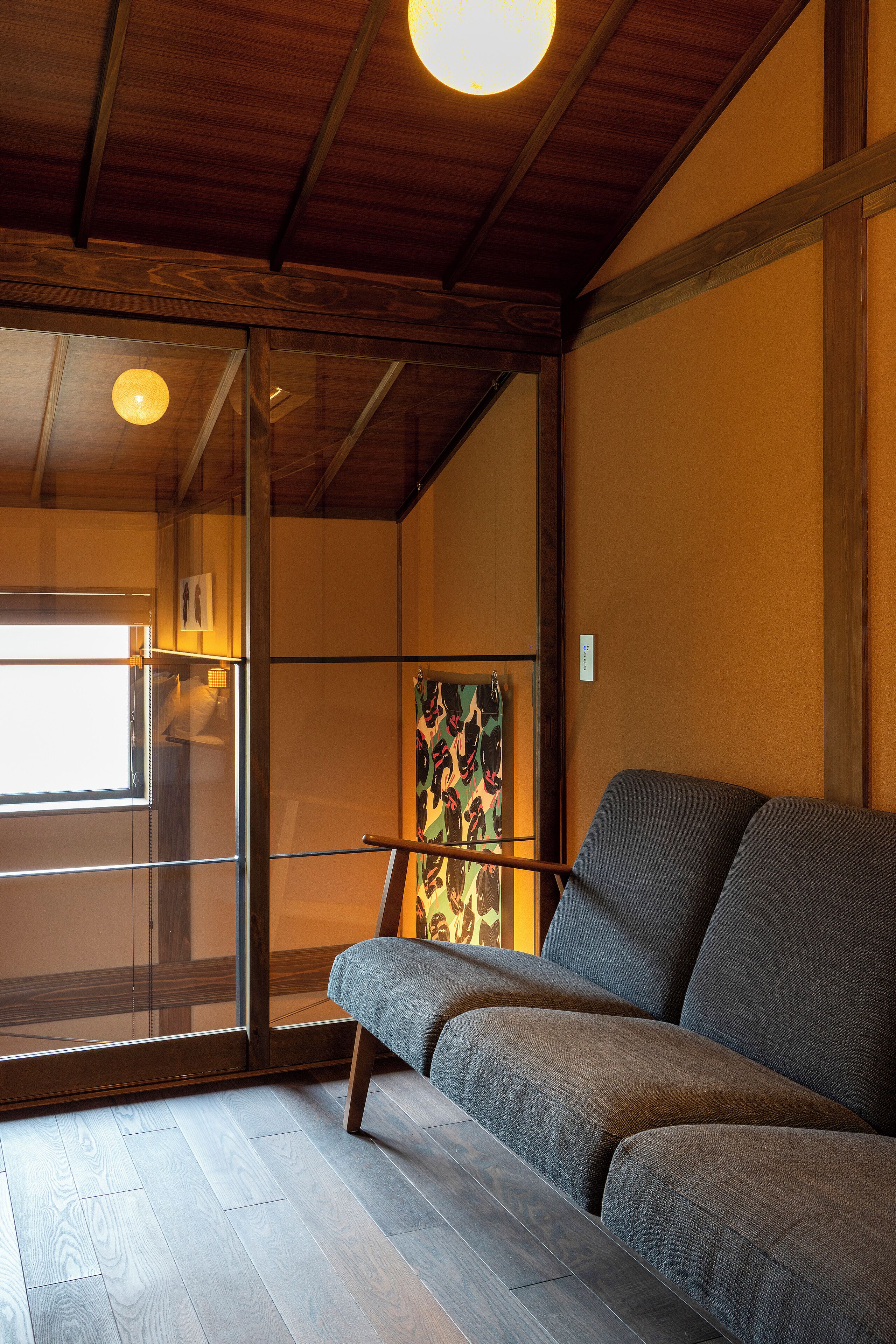 A room with a wooden ceiling, a gray sofa, a glass door leading outside, and a painting on the wall.
