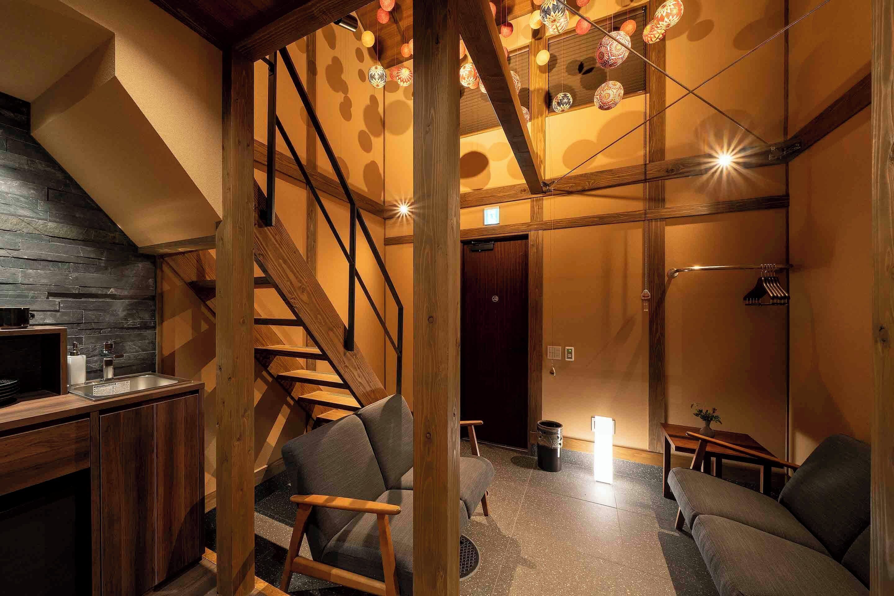 A modern interior with a kitchen area, wooden staircase, and seating space.