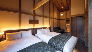 Une chambre d’hôtel avec deux lits, des poutres apparentes, un luminaire fixé au mur et une porte donnant sur une autre pièce.