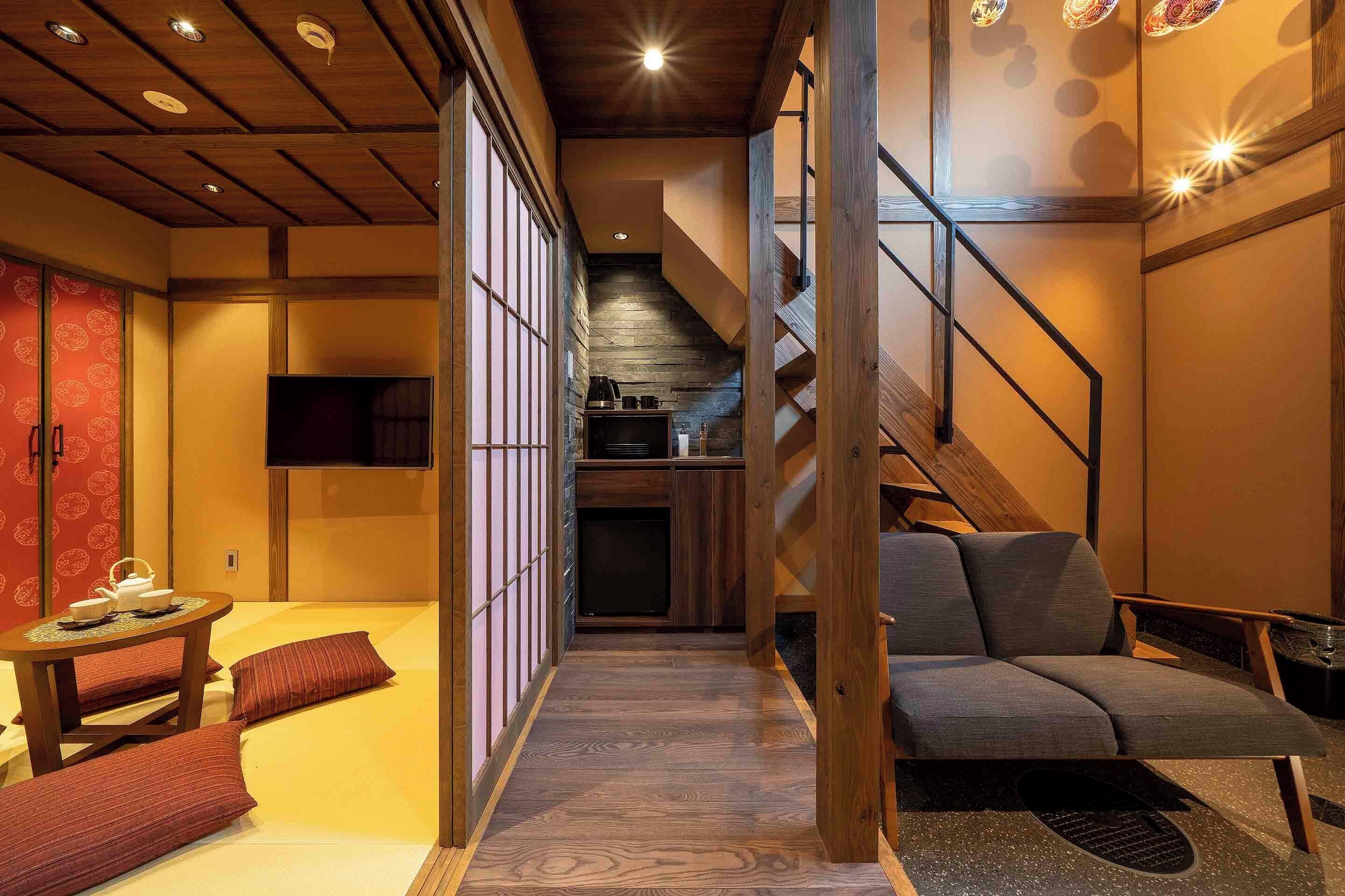 A traditional Japanese-style room with tatami flooring, a low table with a tea set, a sofa, and sliding doors.