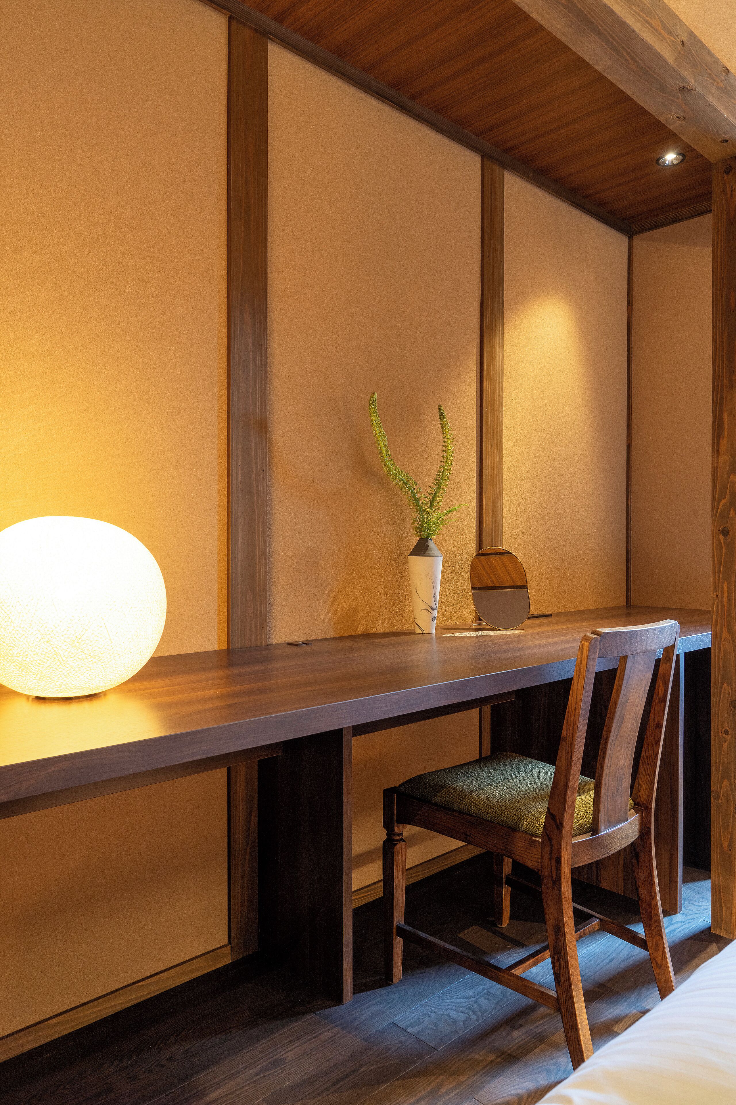 A wooden dining table with a vase of green plants and a round light fixture.