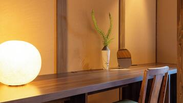 A wooden dining table with a vase of green plants and a round light fixture.