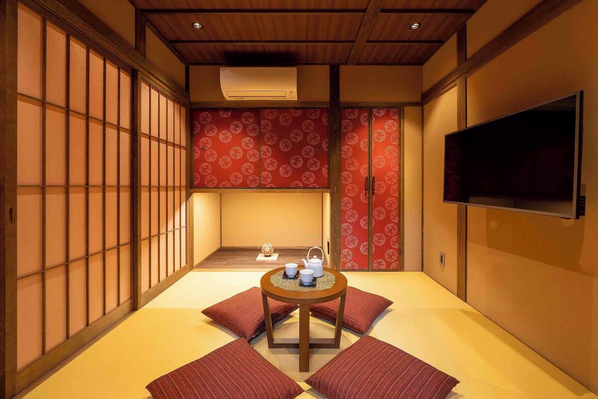 Une pièce de style japonais traditionnel, avec un sol recouvert de tatamis, une petite table sur laquelle est disposé un service à thé, et des portes coulissantes ornées d’un papier peint à motifs rouges.