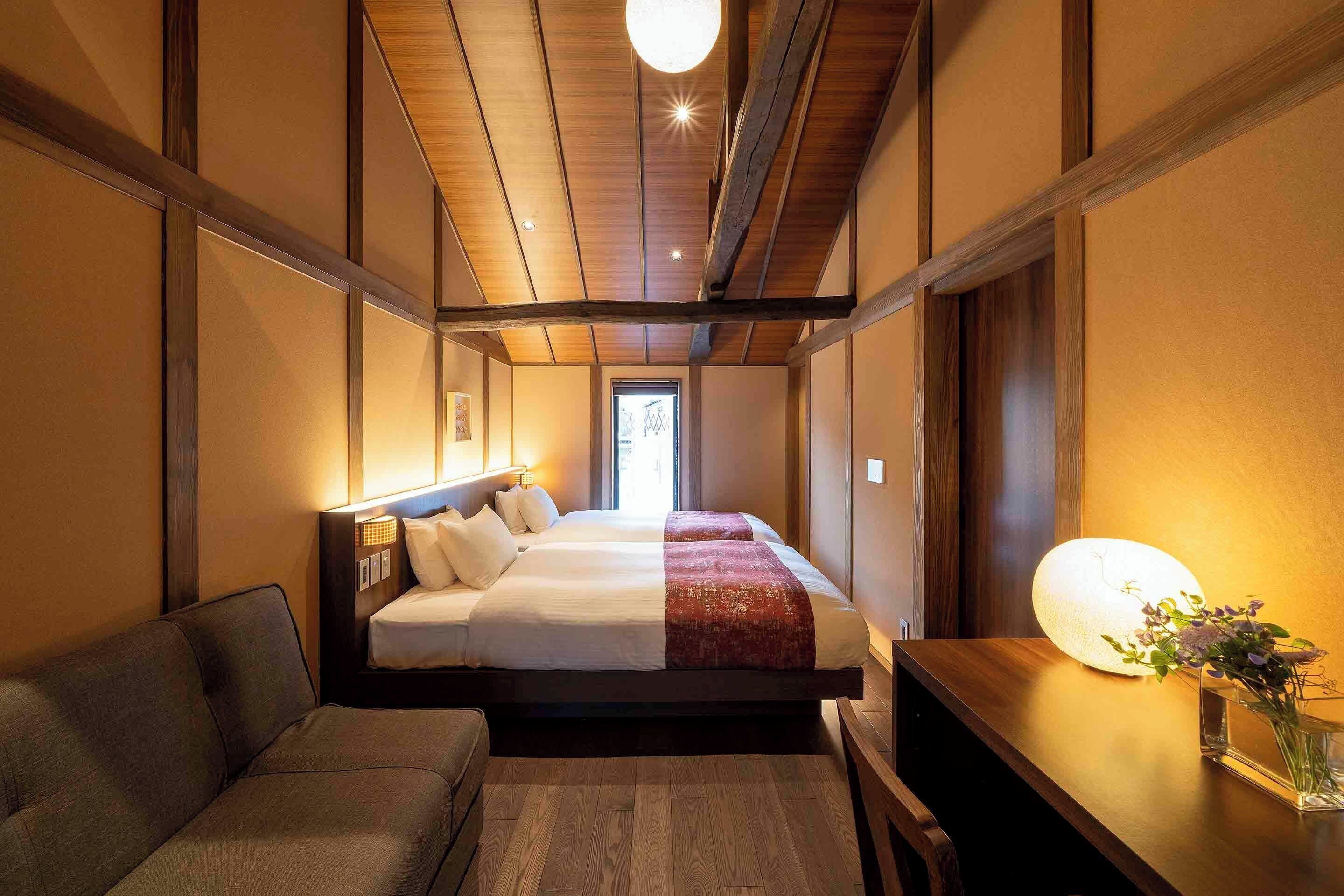 Hotelkamer met een houten plafond, een bed met wit en rode beddengoed, een nachtkastje met een lamp en een kleine tafel met een bloevas.