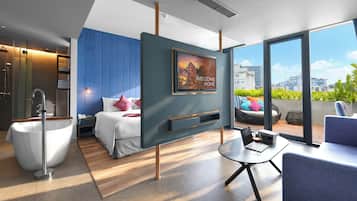 A modern hotel room with a bed, a bathtub, a desk with a laptop, and a large window offering a city view.