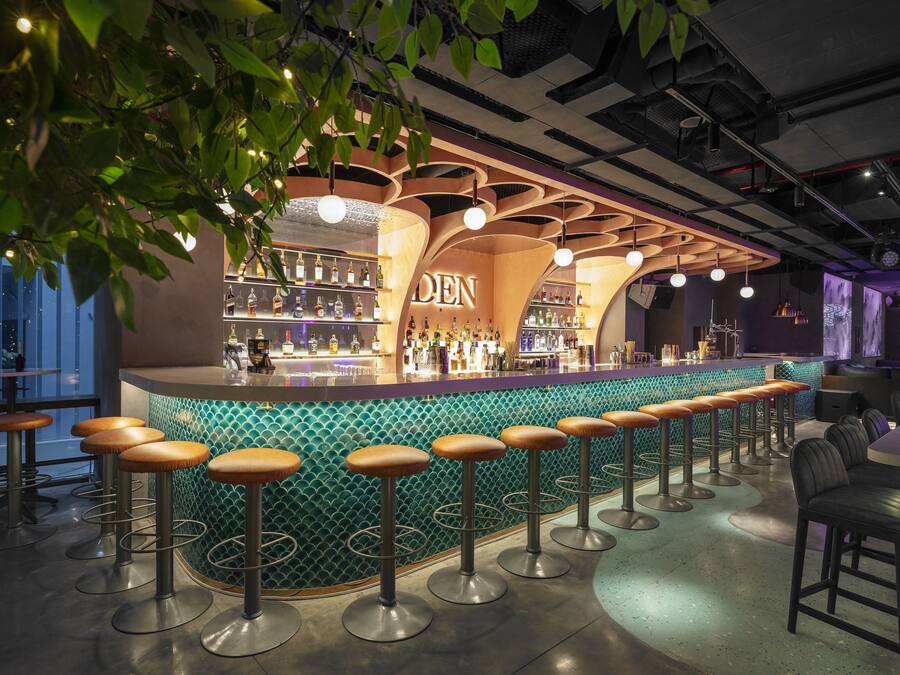 Eine Bar mit einer gebogenen Theke, mehreren Barhocker und Flaschenregalen.