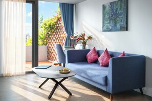 A modern living room with a blue sofa, a glass coffee table, and a dining table with a glass of wine. - HOME Hotel (Ho Chi Minh City)