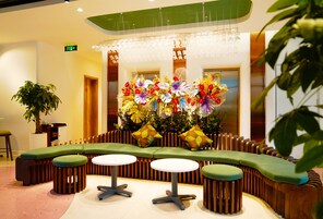 Um lobby moderno com área de estar em curva, um arranjo floral grande e um detalhe no teto verde.