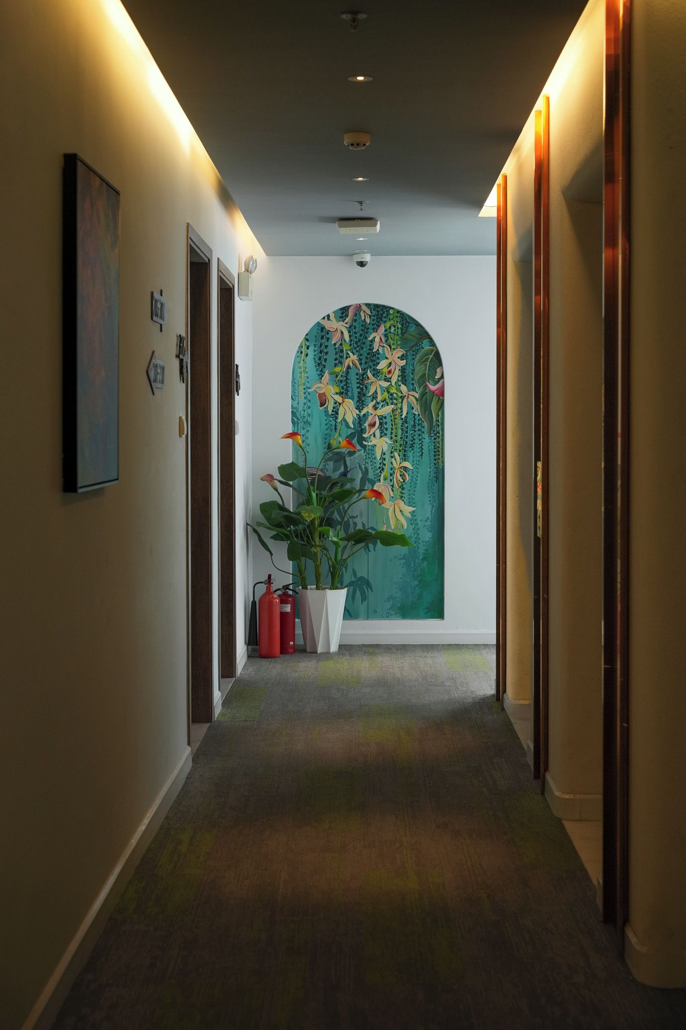 Ein Flur mit Teppichboden, einer Topfpflanze und einer Wand mit floralem Wandbild.