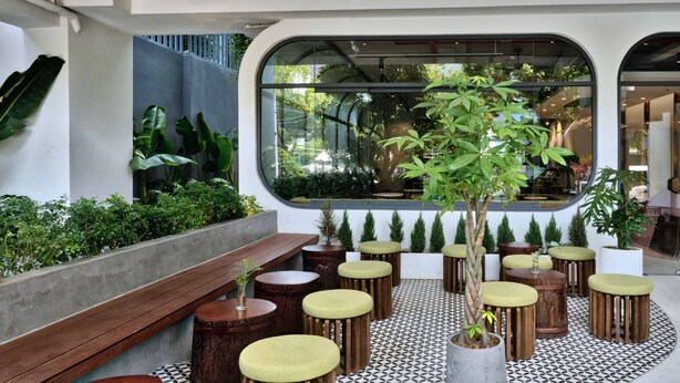 A modern outdoor seating area with wooden stools and benches, surrounded by potted plants and a patterned floor. - HOME Hotel (Ho Chi Minh City)