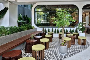 A modern outdoor seating area with wooden stools and benches, surrounded by potted plants and a patterned floor.