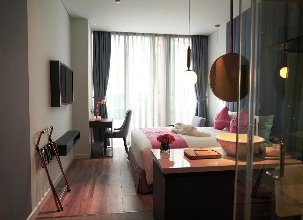 Et hotelværelse med seng, natbord, skrivebord, stol og et vindue med gardiner.