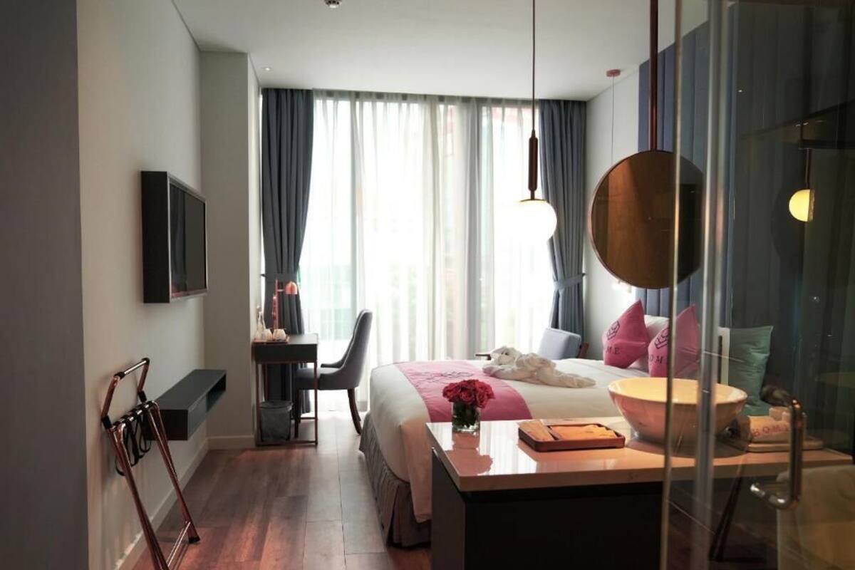 Een hotelkamer met een bed, nachtkastje, bureau, stoel en een raam met gordijnen.