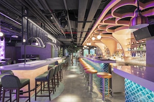 A bar area with a long counter, multiple stools, and a variety of bottles on shelves.