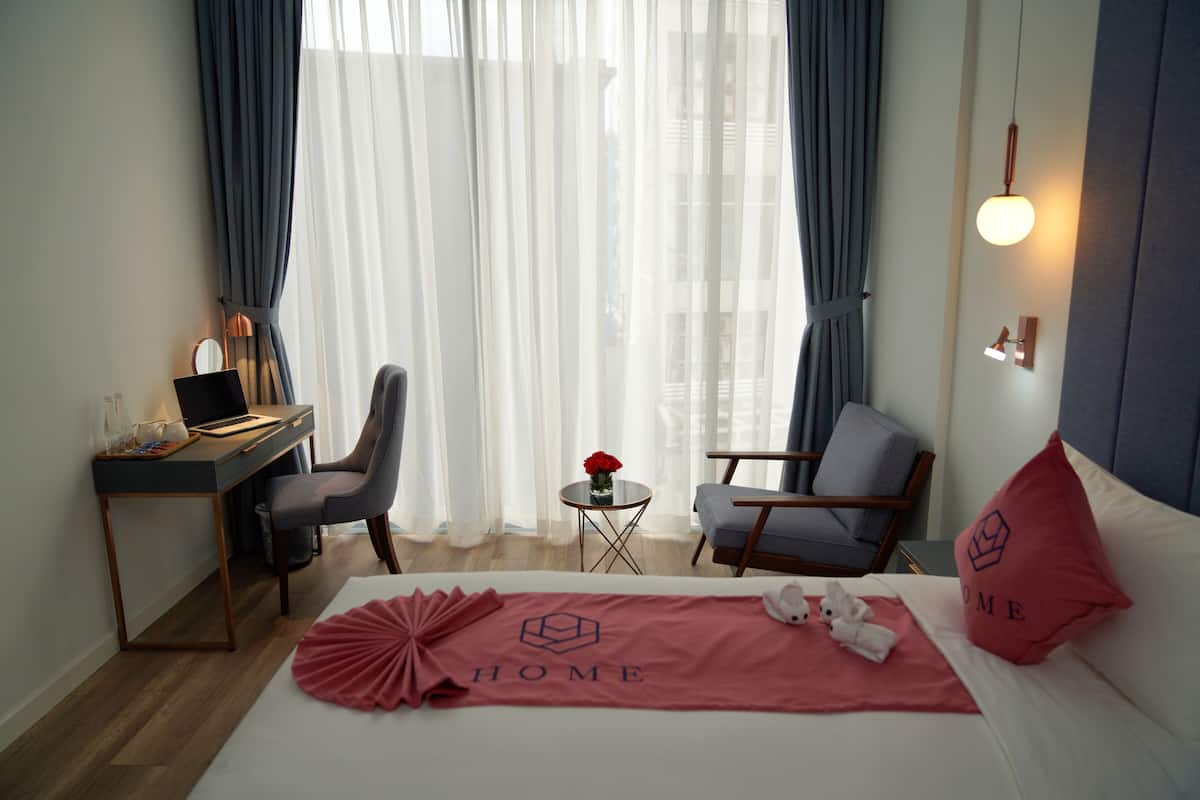 Een hotelkamer met een bed, twee stoelen, een bureau, een klein tafeltje met een bloevas en een lamp.