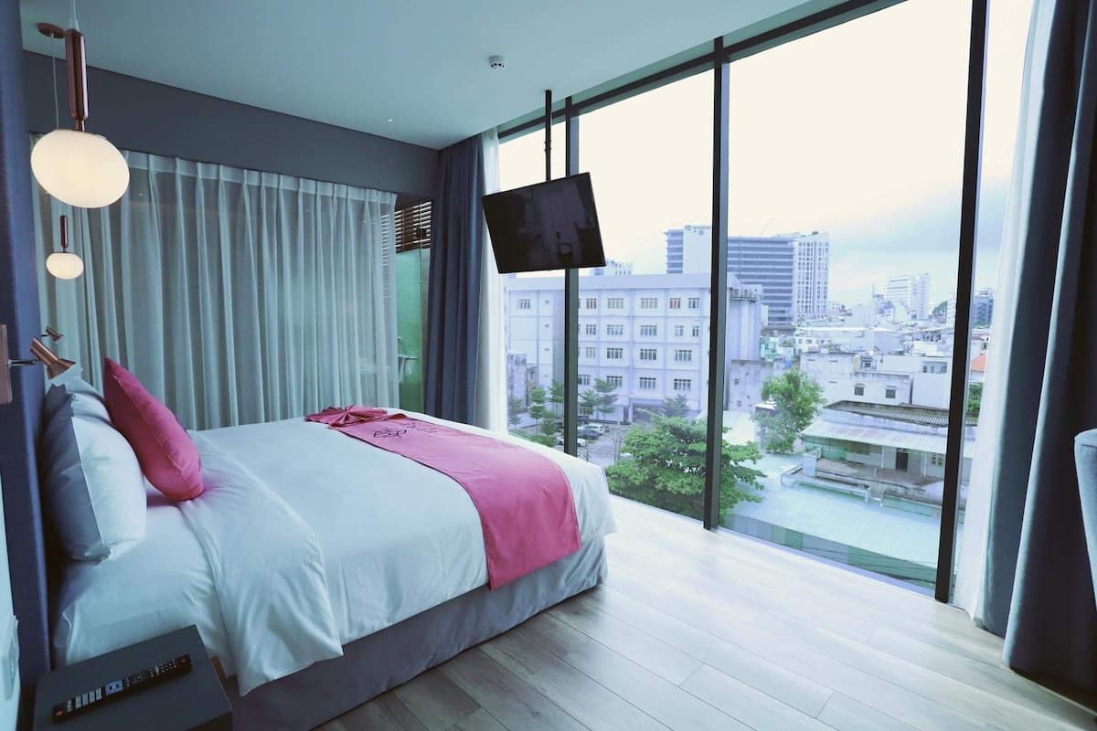 Een moderne hotelkamer met een groot bed, een televisie en uitzicht op de stad door grote ramen.