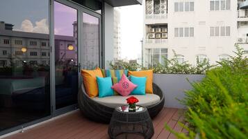 Un balcón con una zona de estar acolchada, una mesa de vidrio con un florero y vistas a un paisaje urbano.