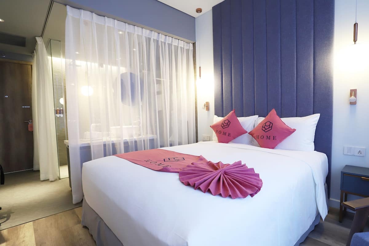 Een hotelkamer met een groot bed, een nachtkastje, een stoel en een raam met dunne gordijnen.