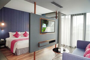 A modern hotel room with a bed, a TV mounted on a wall, a sofa, and a small table.