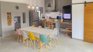 A modern kitchen with a central island, wooden ceiling beams, and a dining area with colorful chairs.