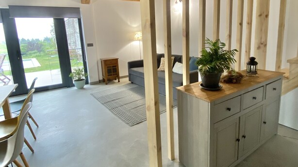 A spacious room with a high ceiling, a dining area with chairs, a sofa, and a wooden cabinet with a plant on top.