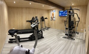 A gym with cardio machines, weightlifting equipment, and a television displaying fitness content.