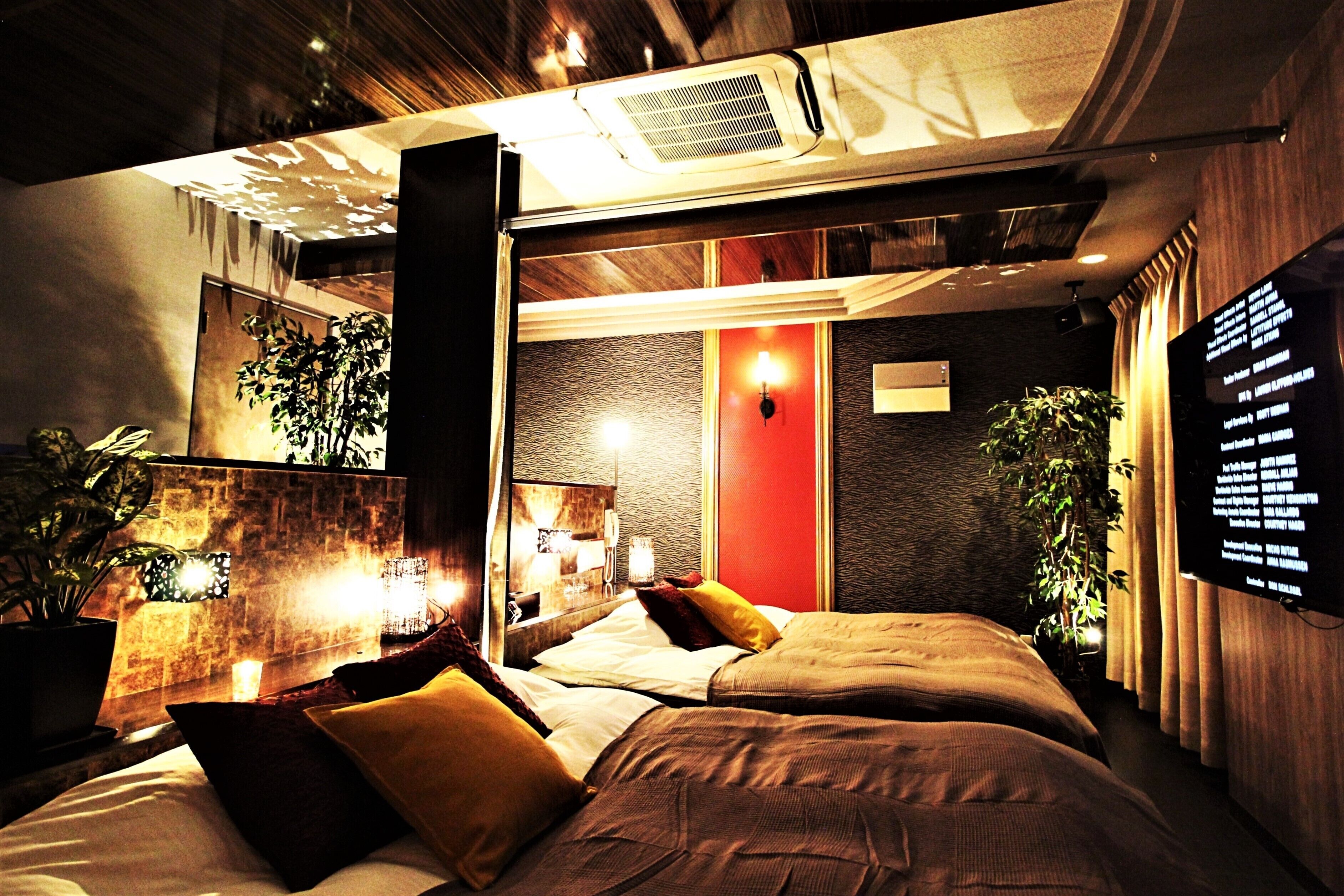 A modern hotel room with a large bed, a red accent wall, and a wall-mounted TV.