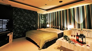 Une chambre d’hôtel avec un lit, une table de chevet sur laquelle se trouvent une bouteille et des verres, une télévision et un mur orné de rayures verticales.