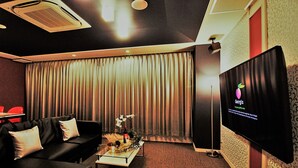 Une chambre d’hôtel avec un canapé en cuir noir, une table basse en verre, un téléviseur à écran plat et une grande fenêtre avec des rideaux.