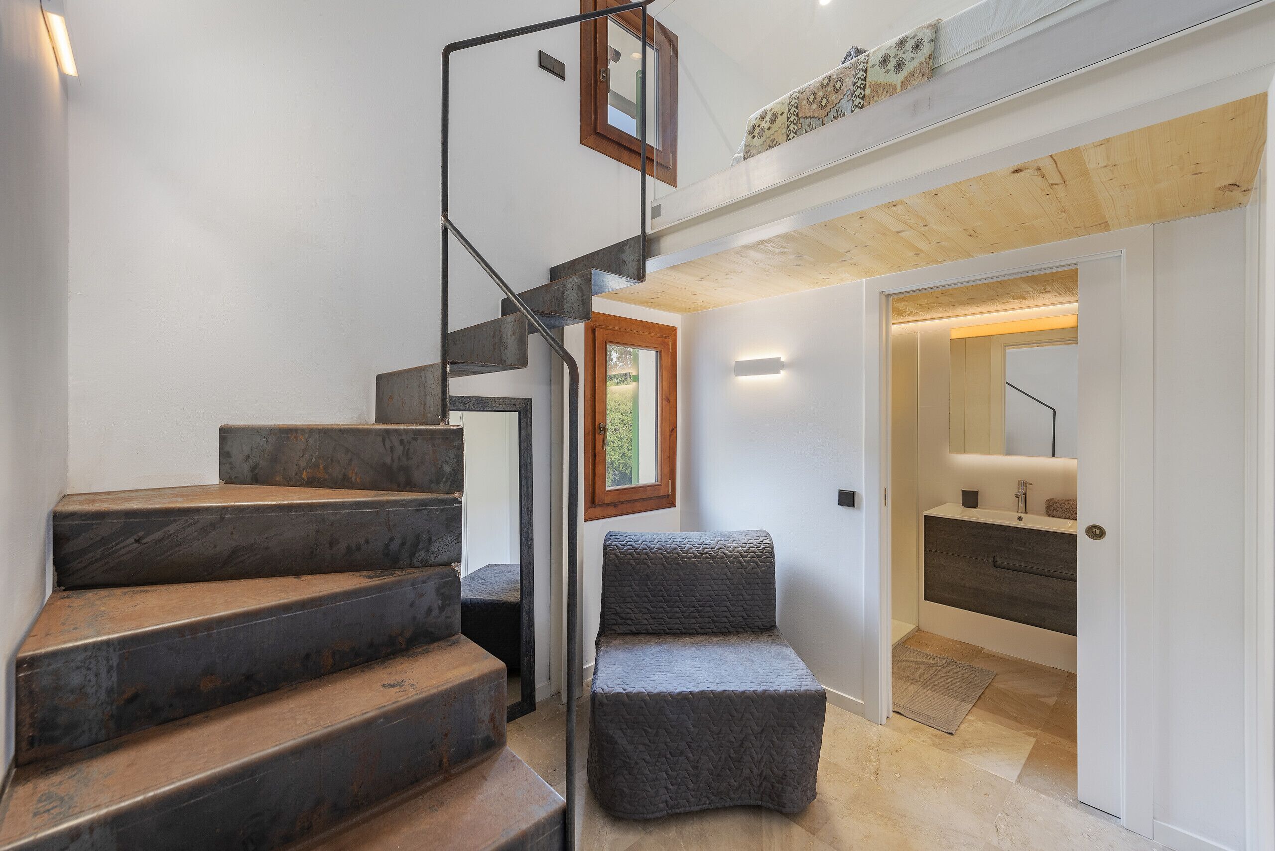 A modern staircase with a metal railing, a wooden ceiling, and a view into a bathroom with a bathtub and a sink.