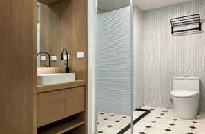 A bathroom with a wooden vanity, a white sink, a black faucet, a toilet, and a hexagonal patterned wall. - Little Inn (Kaohsiung)