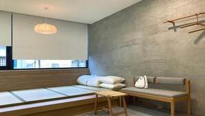 A minimalist room with a low platform bed, a sofa, and a small stool. - Little Inn (Kaohsiung)