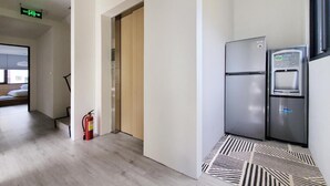 A modern kitchen with a stainless steel refrigerator and water dispenser, a fire extinguisher, and a patterned floor. - Little Inn (Kaohsiung)