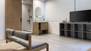 A modern room with a wooden wardrobe, a grey sofa, a small wooden desk, a TV, and a shelving unit. - Little Inn (Kaohsiung)