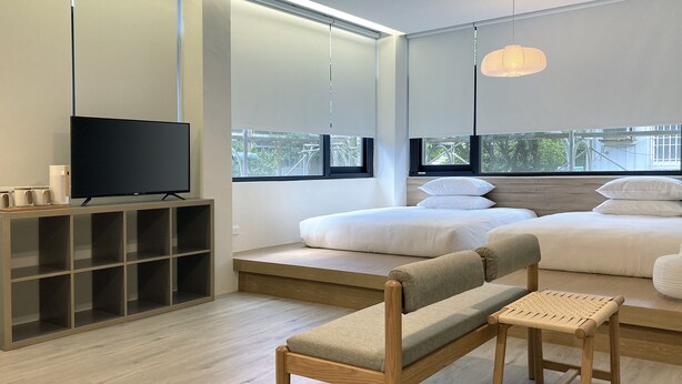 A modern bedroom with a TV, a wooden bench, and a bed with white bedding. - Little Inn (Kaohsiung)
