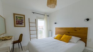 A bedroom with a large bed, a desk, a chair, a ladder, and a window with a view.