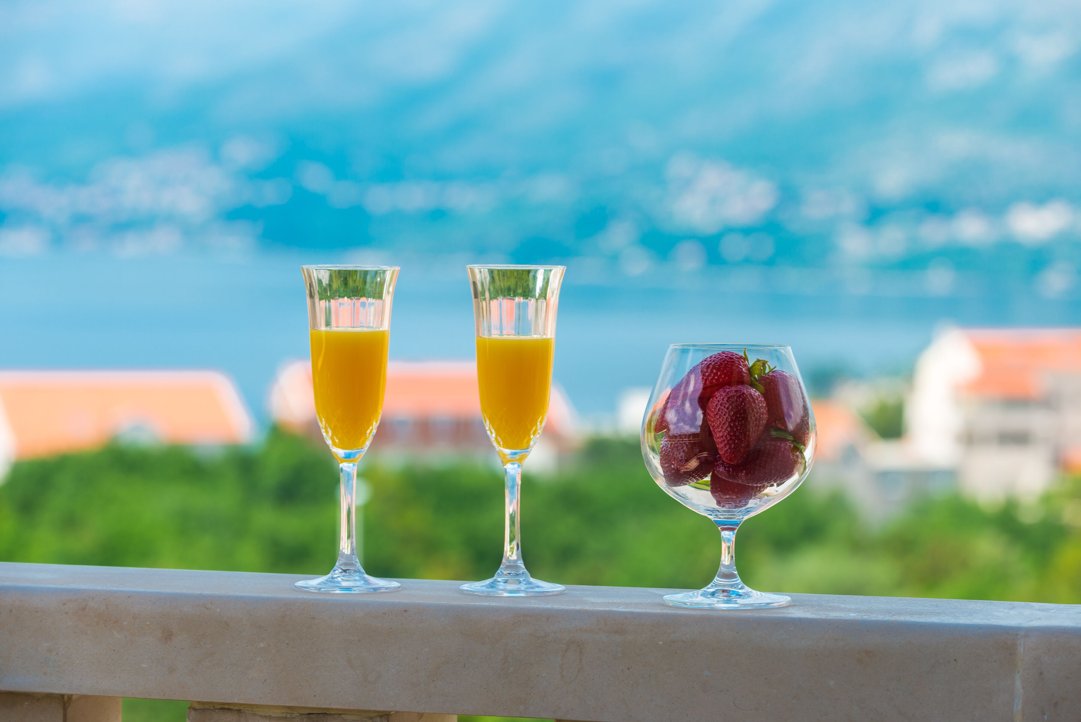 Three glasses of beverages on a balcony with a scenic view.