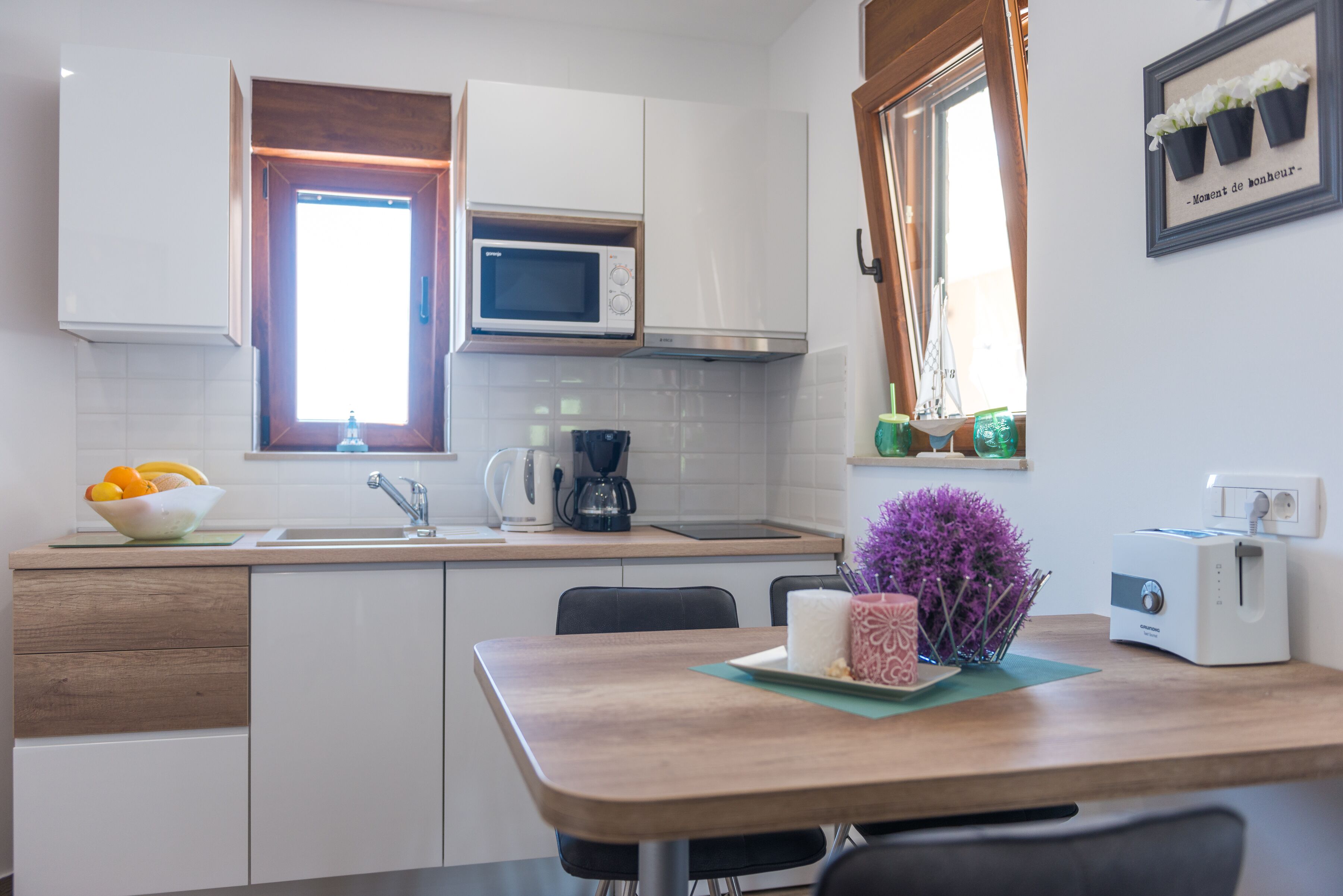 Una cocina moderna con gabinetes blancos, microondas, cafetera y tostadora.