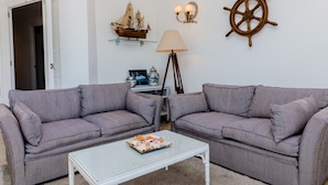 Een woonkamer met twee grijze gestreepte banken, een witte salontafel, een scheepswiel en een scheepsmodel aan de muur.