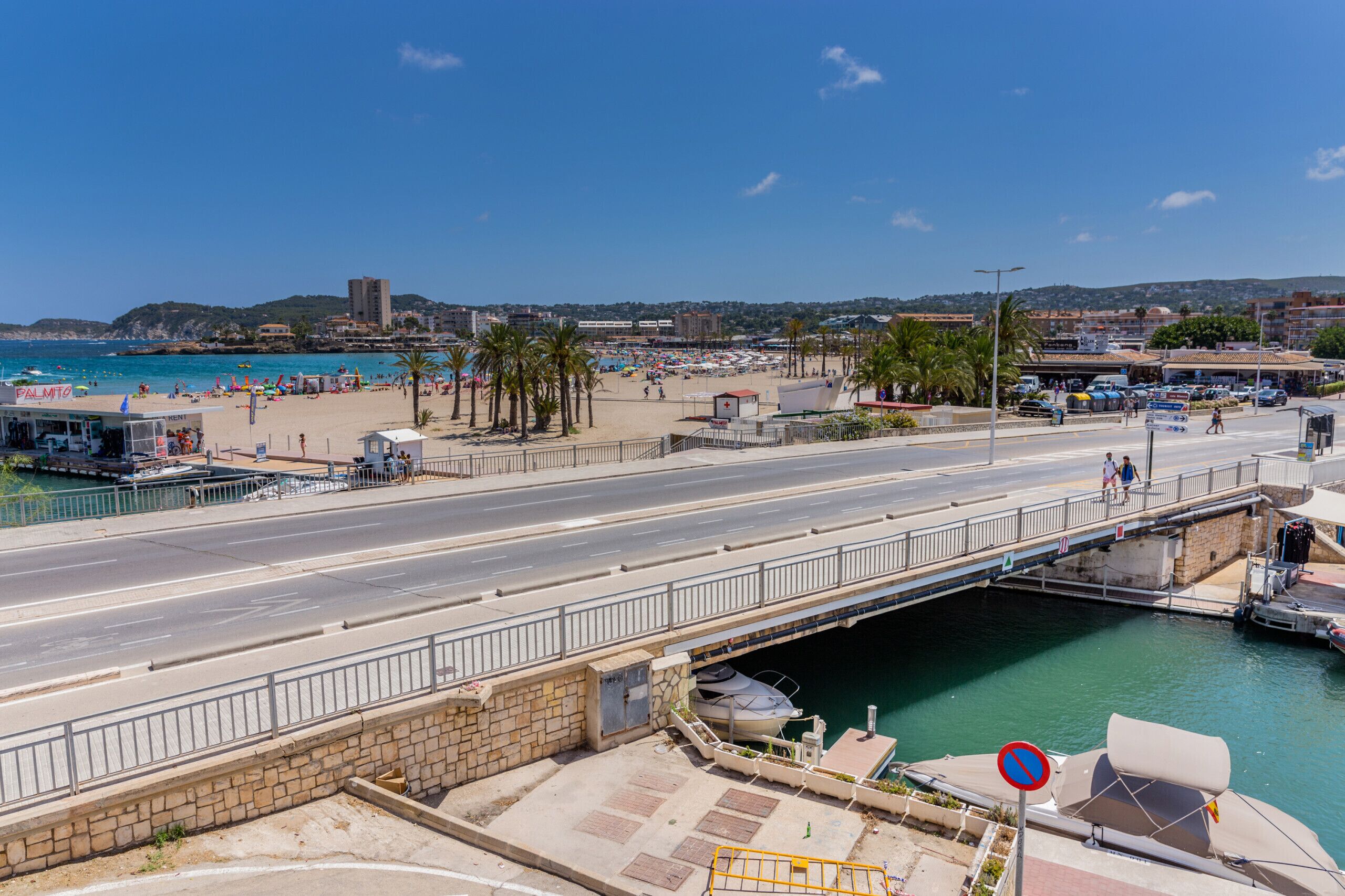 A coastal road with a bridge over a waterway, beach, and beach umbrellas.