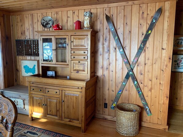 A wooden cabin interior with a wooden cabinet, a red kettle, a map, and skis leaning against the wall.
