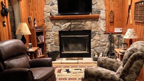 Ein gemütliches Wohnzimmer mit Kamin aus Stein, Ledersesseln und einem flachbildfernseher, der über dem Kamin angebracht ist.