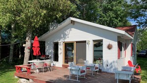 Ein kleines weißes Haus mit einer Terrasse, Sitzgelegenheiten im Freien und einem Grillplatz.