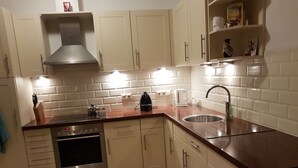 A compact kitchen with white cabinets, a stainless steel range, a built-in oven, a coffee maker, and a sink. - Authentic dike house Nieuw Vliet (Nieuwvliet)