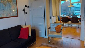 A living room with a black sofa, a red pillow, a map on the wall, and a dining area with a table and chairs. - Authentic dike house Nieuw Vliet (Nieuwvliet)