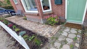 A brick house with a green door, a window with a cushion, and a paved front yard with plants. - Authentic dike house Nieuw Vliet (Nieuwvliet)