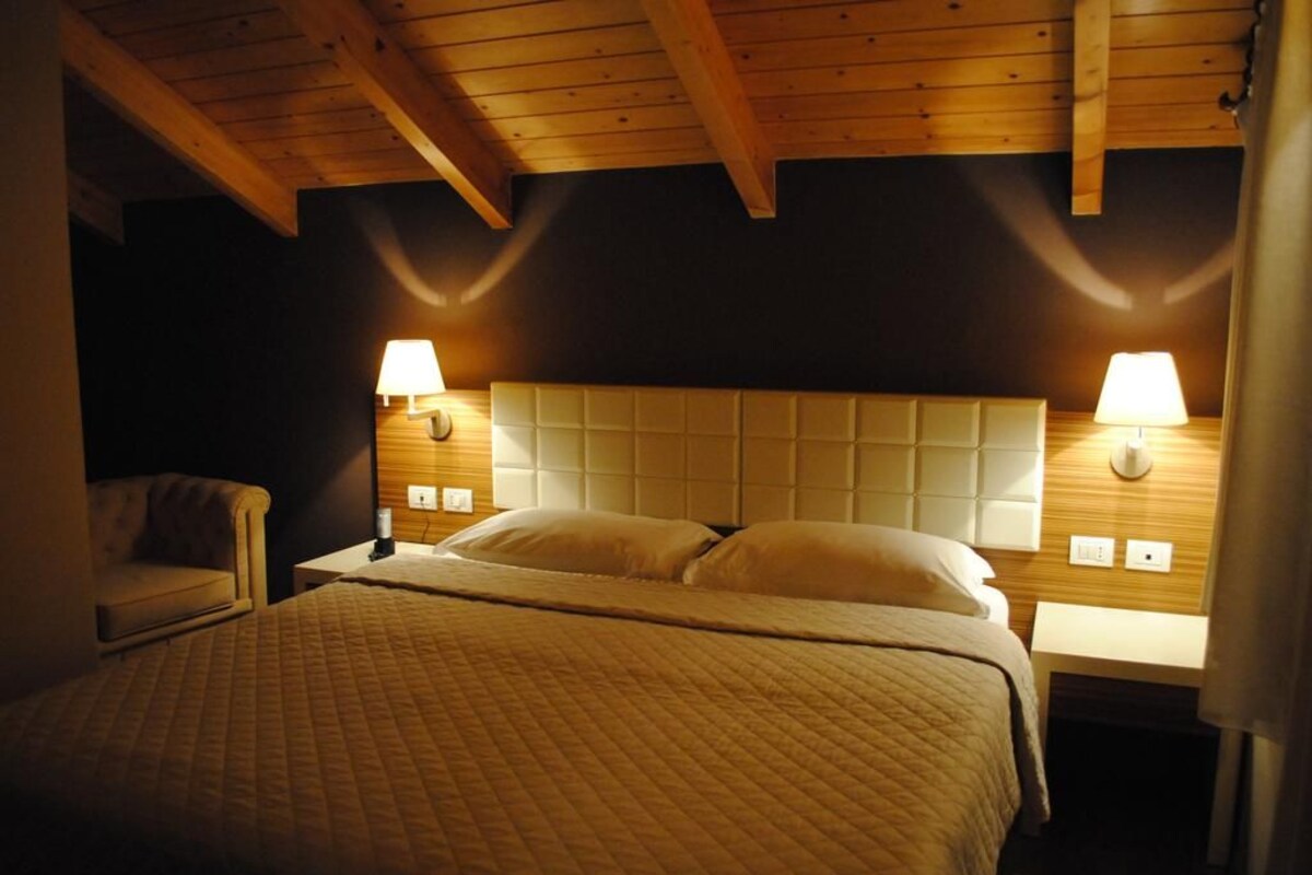 Quarto com uma cama grande, duas luminárias de cabeceira, teto de madeira e uma mesinha de cabeceira.